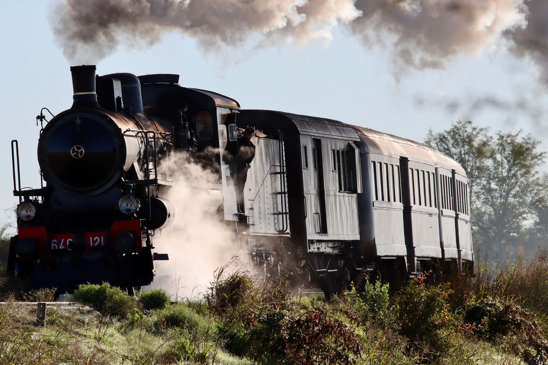 Vintage steam locomotive pulling passenger cars through dry Hill Country grass, like the Hill Country Flyer that runs to Bertram