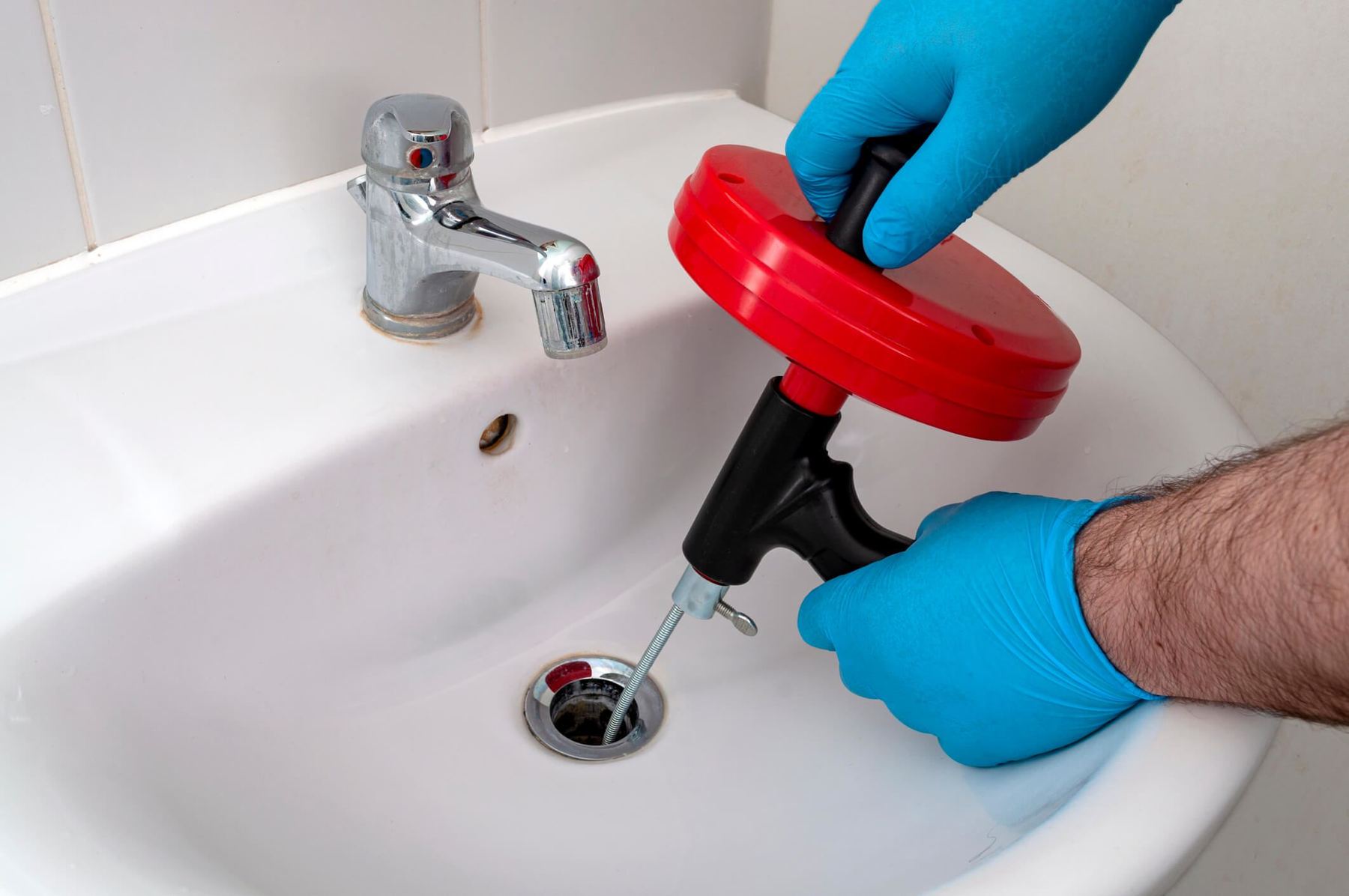 Plumber clearing a bathroom sink drain with a drain snake